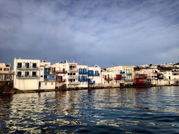 Calm river with houses in background against cloudy sky