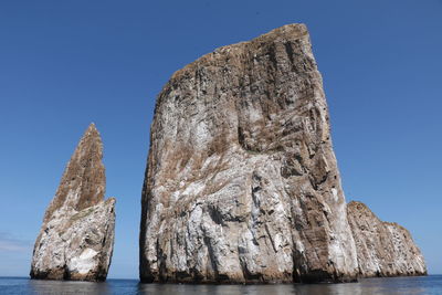 Low angle view of rock formation in sea against clear blue sky