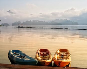 Boats moored on lake against sky during sunset
