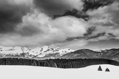 Scenic view of snowcapped mountains against cloudy sky on sunny day