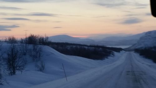 Snow covered landscape against sky during sunset