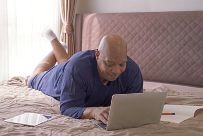 Full length of man using laptop while lying down on bed at home