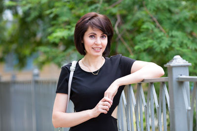 A slender brunette in a black dress with a slit at the waist walks down the street of a sunny city.