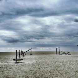 Playground equipment on beach against cloudy sky