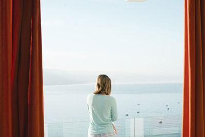 Woman looking at sea while standing in balcony against sky