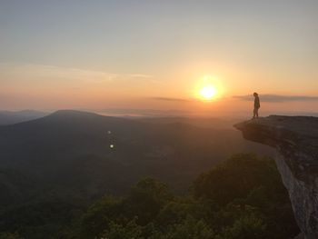 Man standing on cliff against sky during sunset