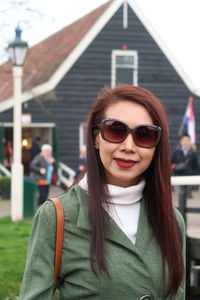 Portrait of woman in sunglasses standing against house