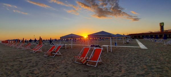 Chairs on beach against sky during sunset