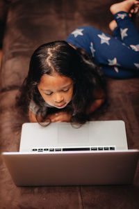 Cute girl using laptop while lying on sofa at home