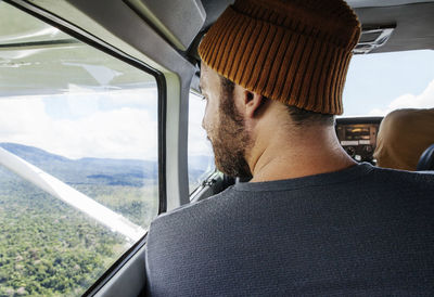 Rear view of man looking through airplane window