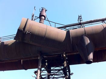 Low angle view of large rusty cut pipe in decommissioned steel mill against clear blue sky