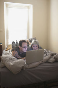 Young couple lying in bed looking at a laptop