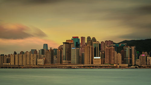 Sea by modern buildings against sky during sunset