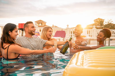 Friends toasting drink glasses in swimming pool