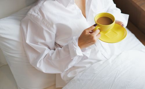 High angle view of woman holding coffee cup on bed