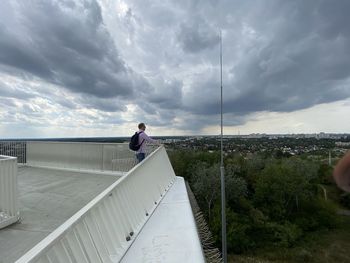 Man standing on railing against sky