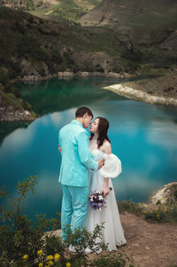 Beautiful wedding couple hugs tenderly against the backdrop of a mountain river and lake, the bride