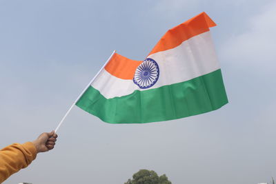 Low angle view of hand holding flag against sky