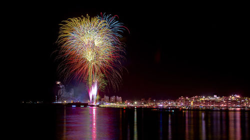 Firework display over illuminated city against sky at night