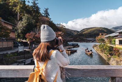 Rear view of woman with umbrella on river against sky