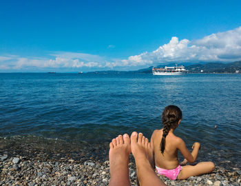 Low section of woman with girl at beach against sky