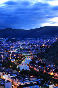 Aerial view of illuminated cityscape against cloudy sky at dusk