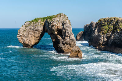 Rocks in sea against clear blue sky