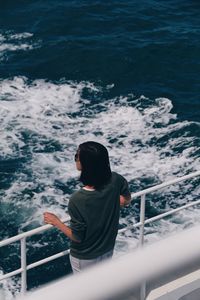 Rear view of woman standing by railing on boat in sea