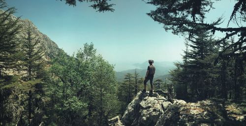 Rear view of man standing on rock while looking at landscape against sky