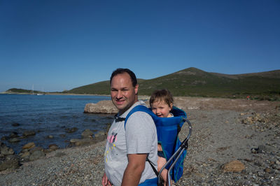 Portrait of man carrying boy in carriage at beach