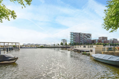 Boats moored on river by buildings in city against sky