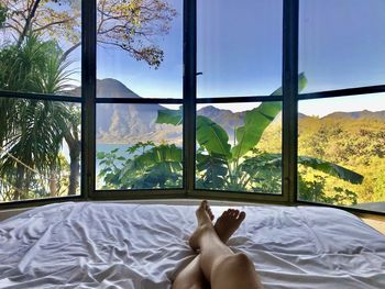 Low section of woman relaxing on bed against window