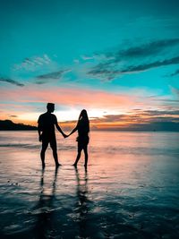 Silhouette couple on beach against sky during sunset