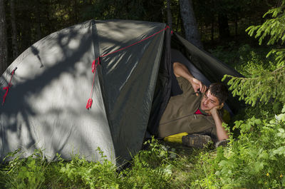 Man lying in tent while talking on cellphone in forest