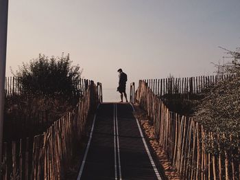 Man walking on footbridge against clear sky