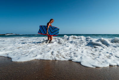 Woman standing on beach against clear blue sky