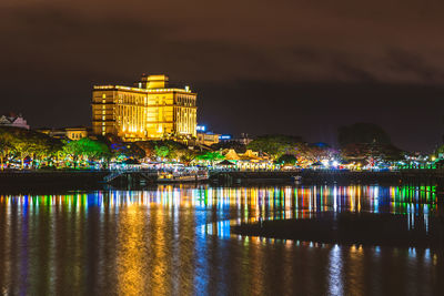 Illuminated waterfront over river against sky at night