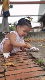 Cute baby girl crouching on footpath