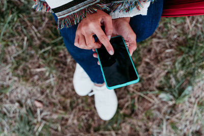 Low section of woman using smart phone while sitting outdoors