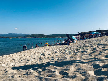 People on beach against clear blue sky