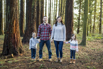 Family holding hands, standing in forest.