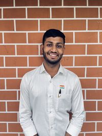 Portrait of smiling young man standing against brick wall
