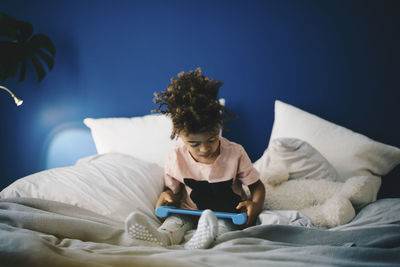 Boy using digital tablet while sitting on bed at home