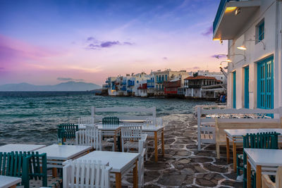 Furniture arranged by sea against sky at sunset