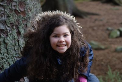 Portrait of smiling girl standing by tree trunk in forest