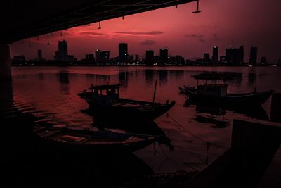 Silhouette boats moored in river by buildings against sky during dusk