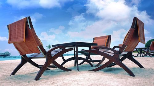 Empty chairs and tables on beach against sky