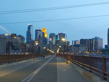 Illuminated street amidst buildings against sky in city