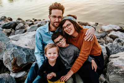 Center portrait of a young family sitting on rocks near a lake