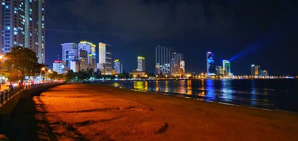 Illuminated city by buildings against sky at night